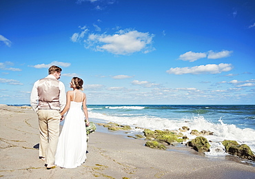 Caucasian bride and groom walking on beach