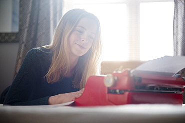 Smiling woman laying on bed typing on typewriter