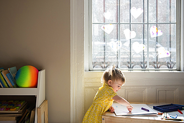 Caucasian baby girl coloring on sketchpad near window