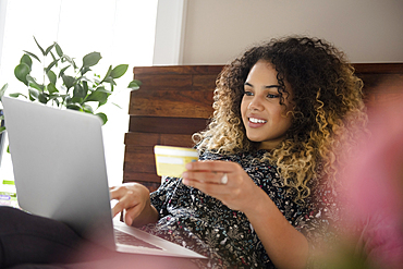 Mixed Race woman laying on bed online shopping with laptop