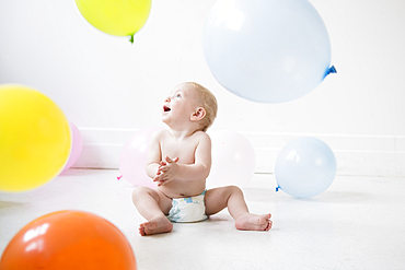 Caucasian baby boy sitting on floor watching balloons