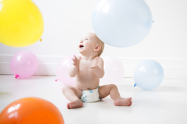 Caucasian baby boy sitting on floor watching balloons