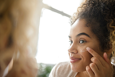 Mixed Race woman applying lotion to cheek