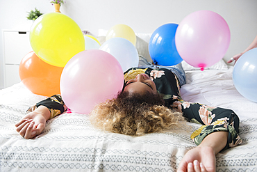 Mixed Race woman sitting on bed covered with balloons