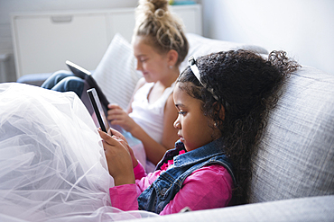 Girls using digital tablets on sofa