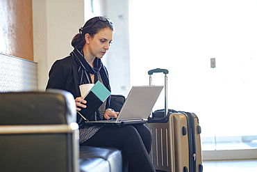 Hispanic woman holding passport using laptop in airport