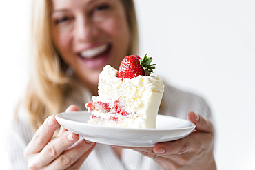 Caucasian woman holding slice on vanilla cake with strawberry