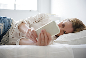 Caucasian woman laying on bed texting on cell phone