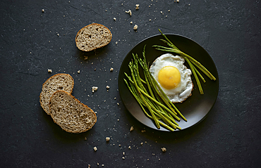 Bread and crumbs near plate with fried egg and asparagus