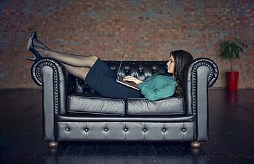 Caucasian businesswoman laying on sofa using digital tablet