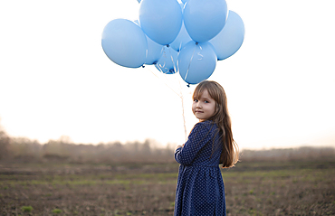 Caucasian girl holding blue helium balloons