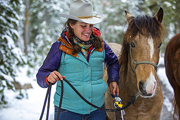 Smiling Caucasian woman holding rein of horse in winter