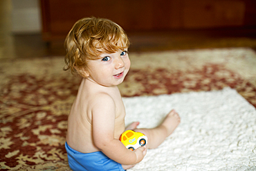 Caucasian baby boy sitting on rug holding toy car