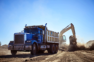 Truck near digger in dirt field