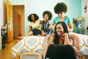 Woman braiding hair of friend in bedroom