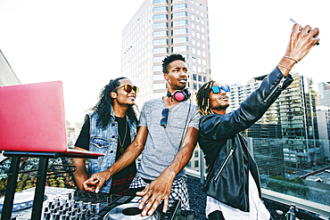 Men posing for cell phone selfie with DJ on urban rooftop