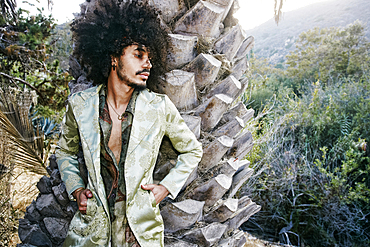 Mixed Race man wearing jacket leaning on tree trunk