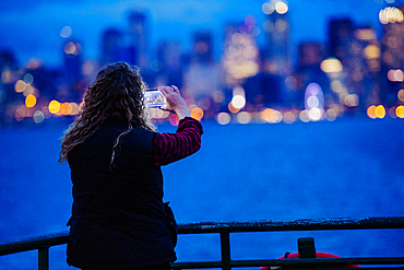 Caucasian woman on boat photographing urban waterfront with cell phone