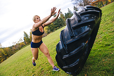 Caucasian woman pushing heavy tire up hill