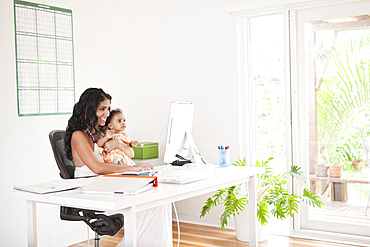 Mixed Race mother using computer and holding baby daughter