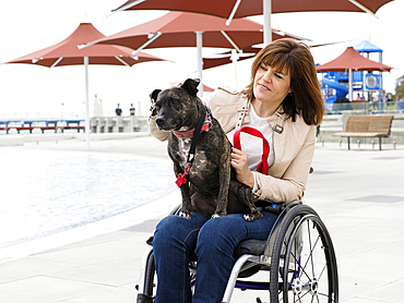 Woman sitting in wheelchair at waterfront with dog in lap