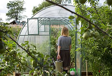 Caucasian woman carrying watering can to greenhouse