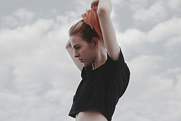 Caucasian woman arranging hair against clouds