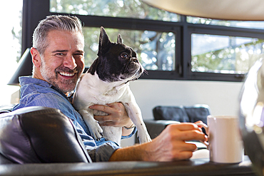 Caucasian man hugging dog on sofa and drinking coffee