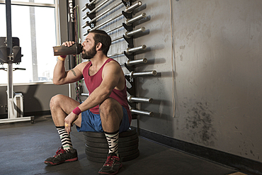 Mixed Race man drinking from bottle in gymnasium