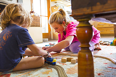 Caucasian brother and sister playing with toy race track on floor