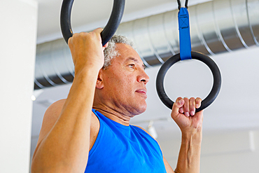 Mixed Race man using pull-up rings in gymnasium