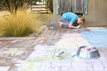 Caucasian girl drawing with chalk on patio bricks