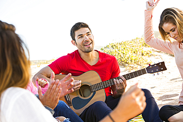 Man playing guitar for friends at beach