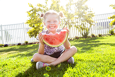 Caucasian girl sitting in grass eating watermelon