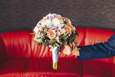 Caucasian man holding bouquet of flowers near red sofa