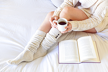 Caucasian woman reading book on bed and drinking coffee