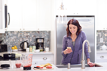 Caucasian woman texting on cell phone in domestic kitchen