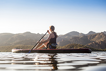 Caucasian woman sitting on paddleboard in river