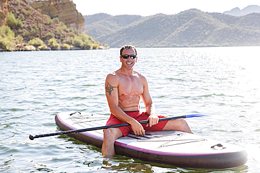 Hispanic man sitting on paddleboard in river