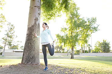 Caucasian woman leaning on tree stretching leg