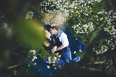 Caucasian couple laying in grass under flowering trees