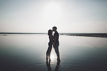 Caucasian couple wading in lake and kissing