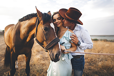 Caucasian cowboy kissing woman on cheek near horse