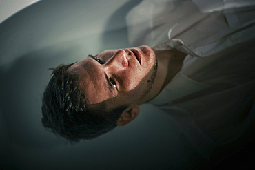 Caucasian man wearing shirt floating in bathtub water