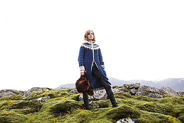 Caucasian woman standing on mossy rocks holding fur hat