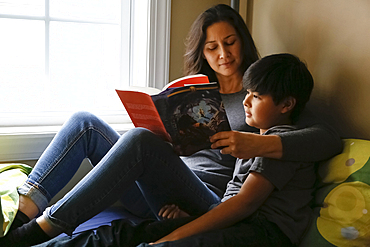 Mother and son reading book near window