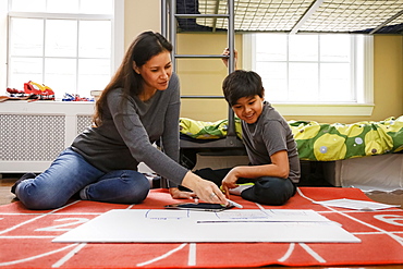 Mother and son sitting on floor of bedroom drawing on placard