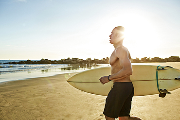 Mixed race man running with surfboard on beach