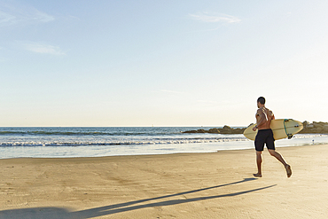 Mixed race man running with surfboard on beach