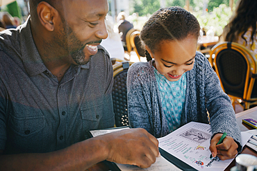 Father watching daughter coloring with crayon in restaurant